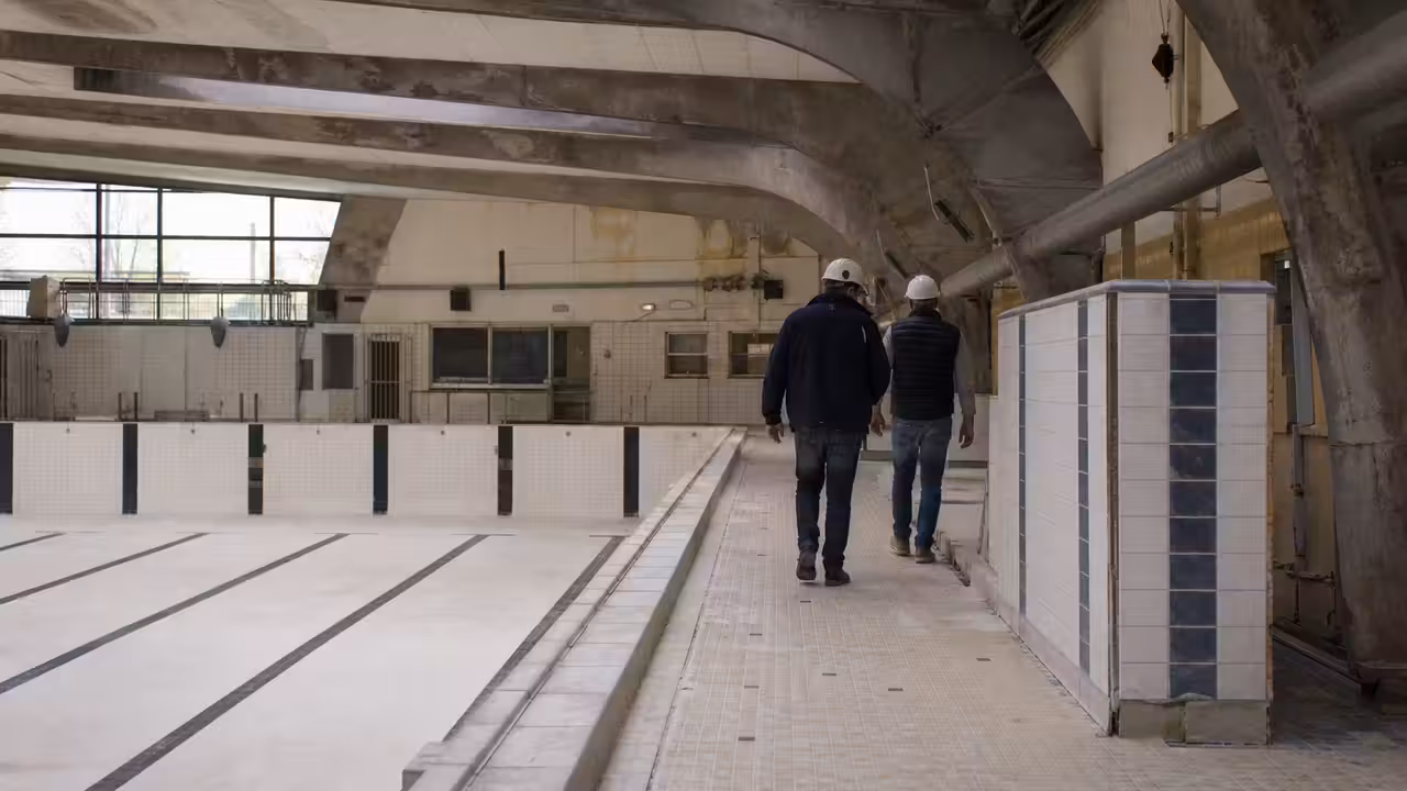 Bassin couvert de piscine municipale en rénovation avec couloirs de nage et équipements techniques en arrière-plan