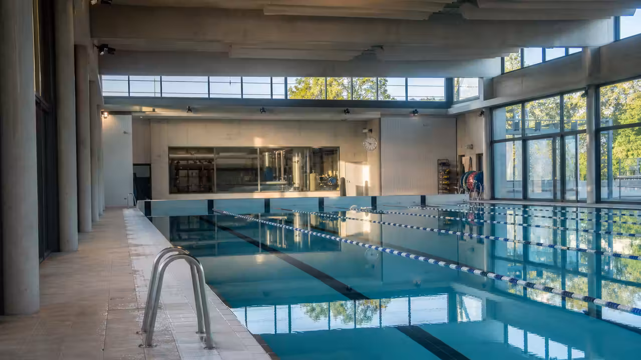 Vue extérieure d’un centre aquatique moderne en chantier, avec structure vitrée et aménagements urbains