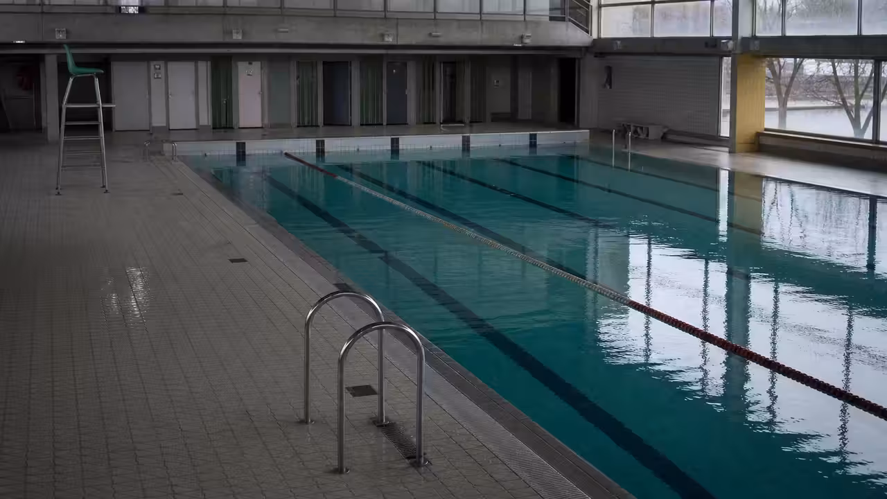 Bassin intérieur d’une piscine municipale avec lignes d’eau, gradins sobres et lumière naturelle latérale