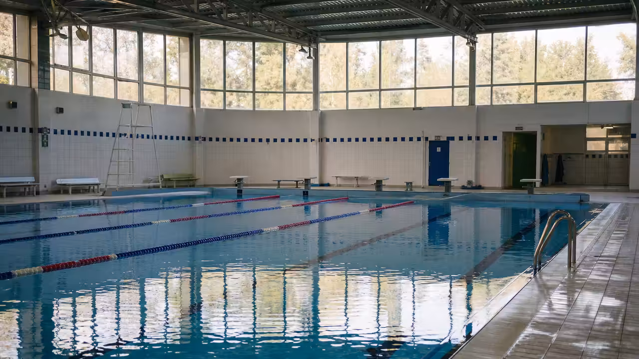 Bassin intérieur d’une piscine municipale vide, avec lignes d’eau et lumière naturelle sur le carrelage.