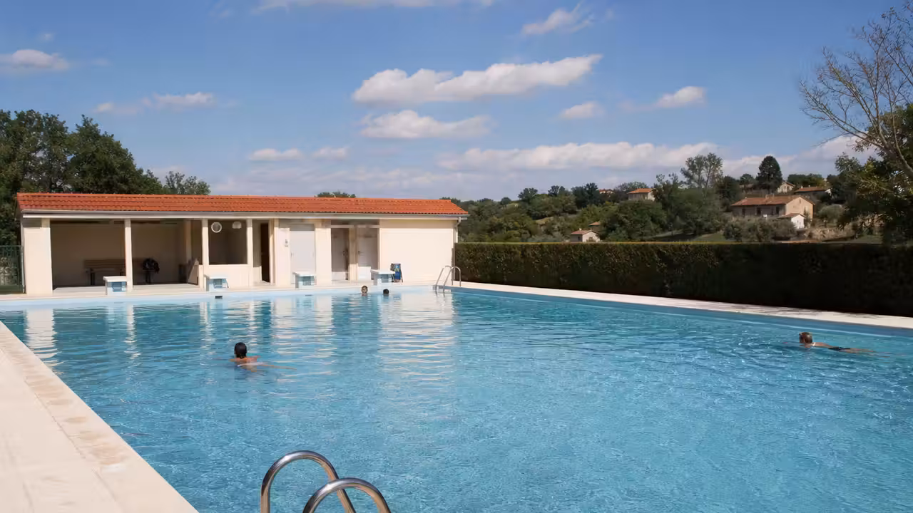 Bassin extérieur d’une piscine municipale en milieu rural, avec plages minérales et eau calme en été