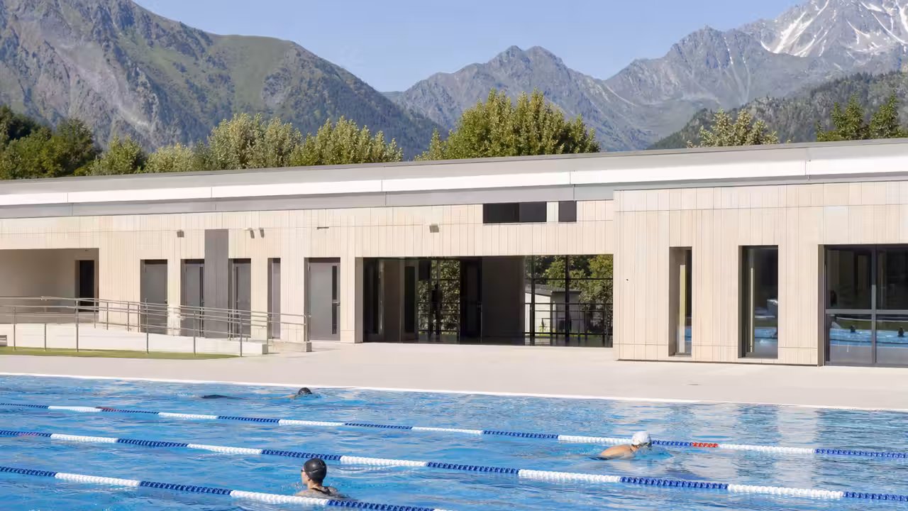 Bassin municipal rénové avec lignes d’eau, vestiaires lumineux et reliefs alpins visibles au loin