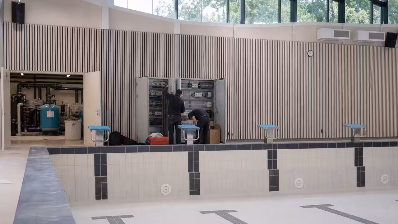 Bassin municipal rénové vu depuis la plage, avec lignes d’eau, gradins et équipements techniques discrets