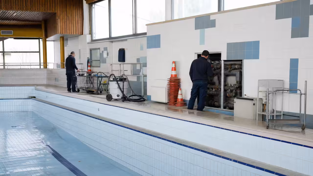 Bassin municipal vide pendant un entretien technique, avec carrelage, canalisations et matériel de maintenance