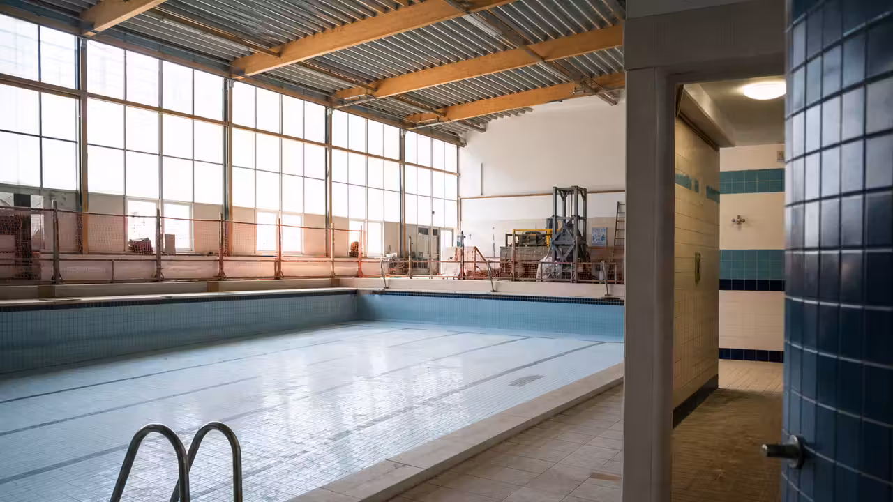 Couloirs d’un bassin municipal vide pendant une rénovation, avec vestiaires et lumière naturelle en arrière-plan