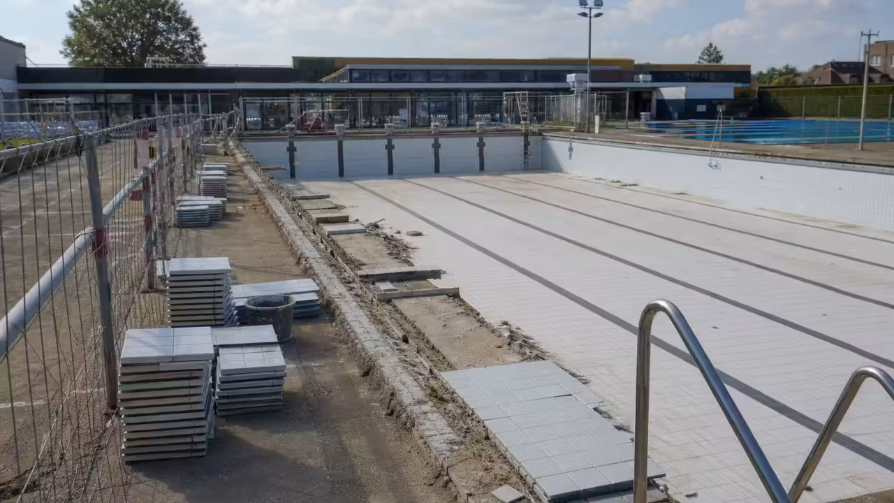 Bassin extérieur d’une piscine municipale en rénovation, avec zones de chantier sécurisées et gradins vides