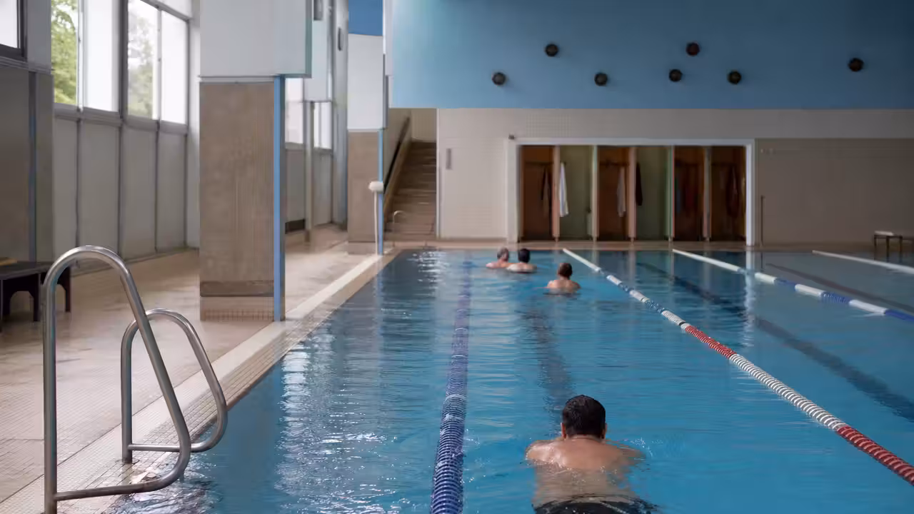 Intérieur lumineux d’une piscine municipale parisienne avec lignes d’eau, vestiaires au fond et nageurs de dos