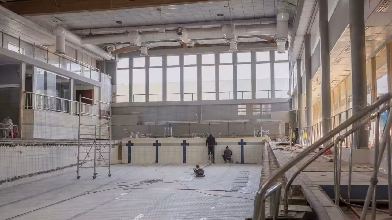 Bassin intérieur municipal vide pendant des travaux, avec échafaudages et réseaux techniques visibles