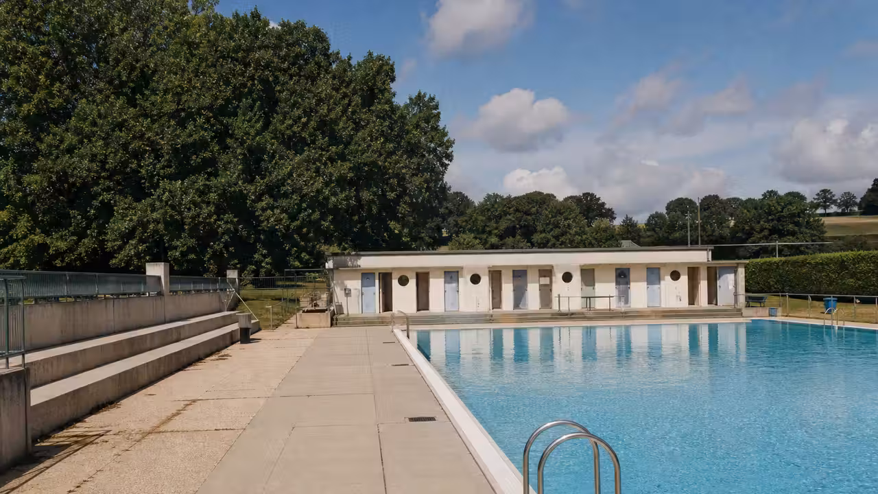 Vue extérieure d’un équipement aquatique municipal entouré d’arbres, avec bassin et plages au premier plan