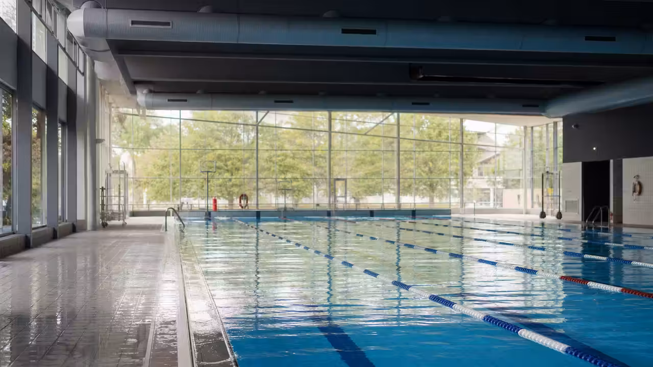 Bassin intérieur d’un centre aquatique municipal avec lignes d’eau, baies vitrées et gradins vides