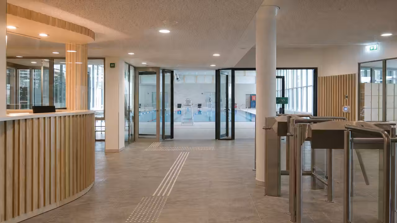 Hall lumineux d’un centre aquatique public avec portiques d’accès, guichet et signalétique accessible