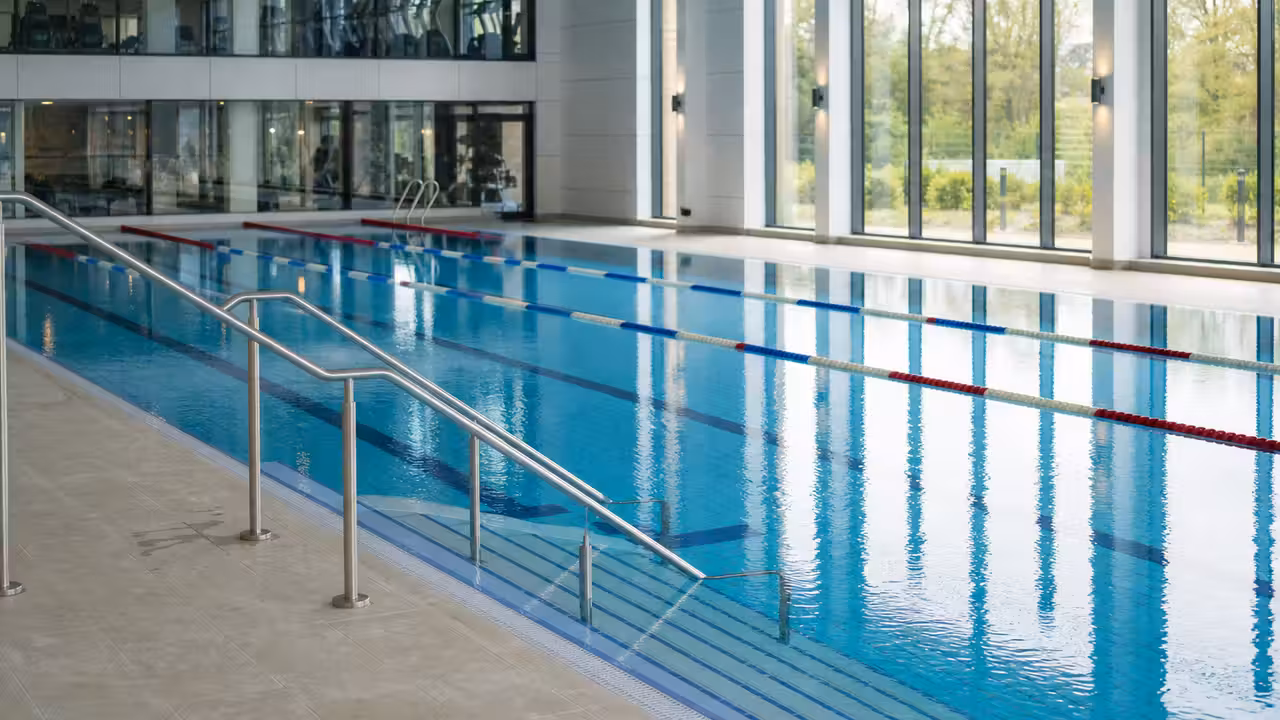 Bassin couvert de 25 mètres avec lignes d’eau, baies vitrées et espace fitness en arrière-plan
