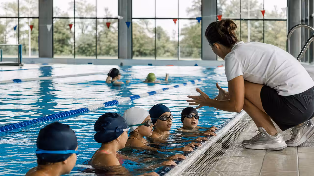 Maître-nageur encadrant un petit groupe d’apprentis nageurs dans une piscine publique lumineuse