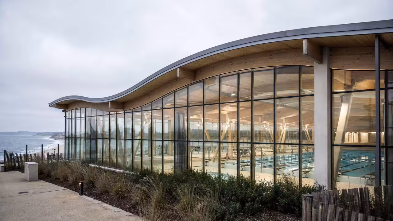Bassin sportif couvert de 50 mètres, lignes d’eau et grandes baies vitrées dans un centre aquatique