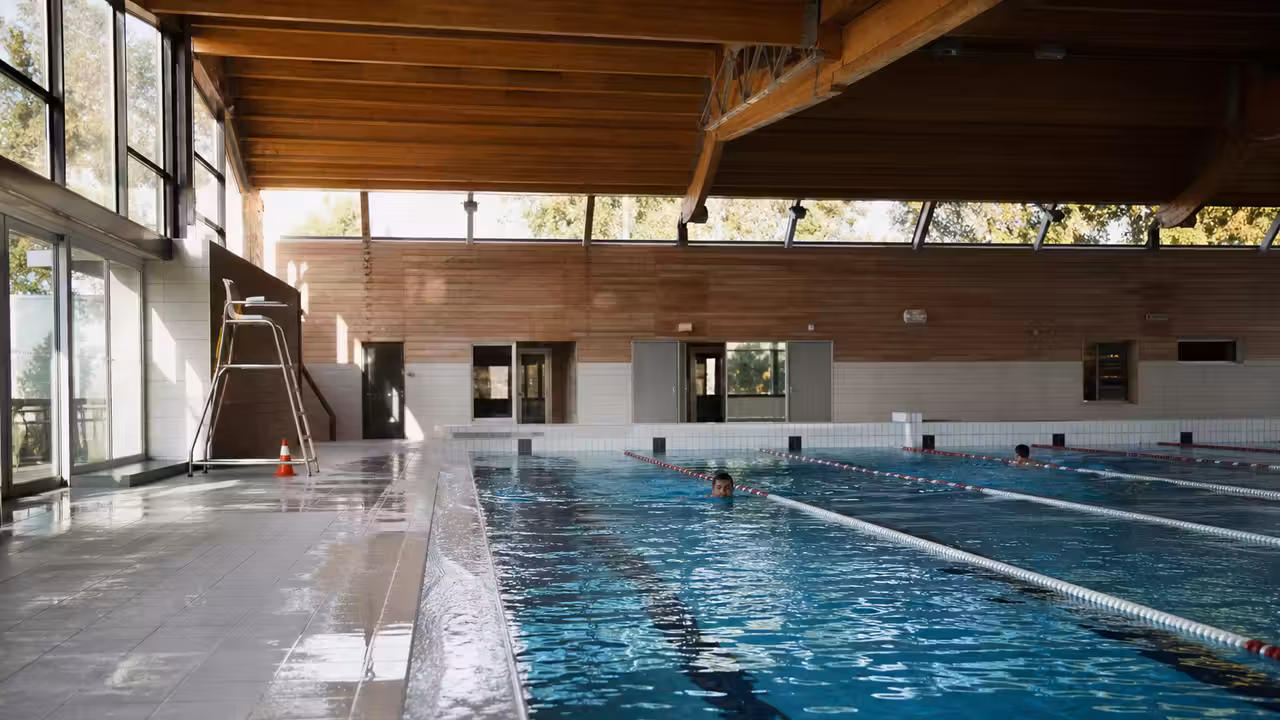 Bassin intérieur d’une piscine municipale avec lignes de nage, vestiaires et lumière naturelle de fin de journée