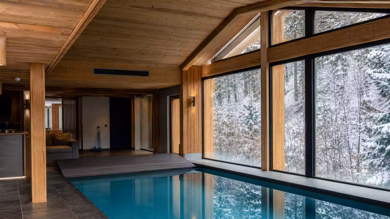 Bassin intérieur dans un chalet de montagne, avec bois clair, pierre naturelle et grandes baies sur les sapins