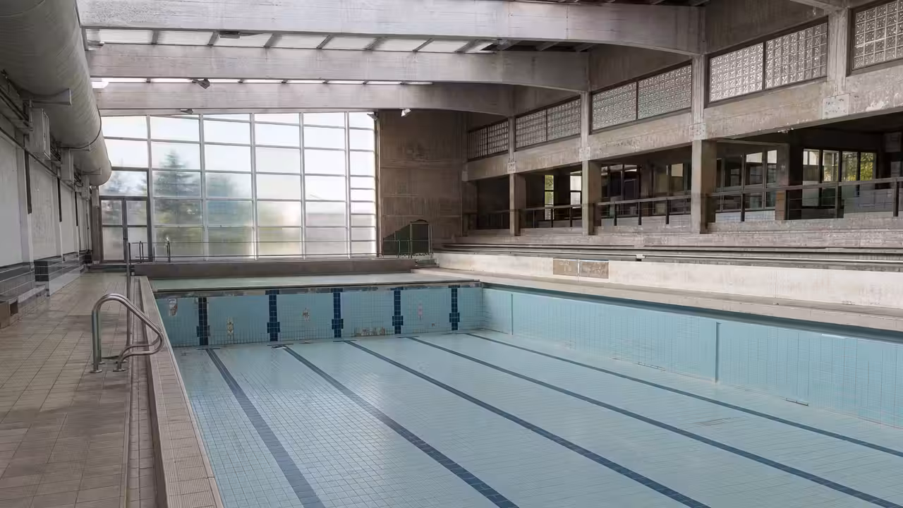 Bassin couvert municipal vide, avec charpente métallique, baies vitrées et équipements techniques rénovés