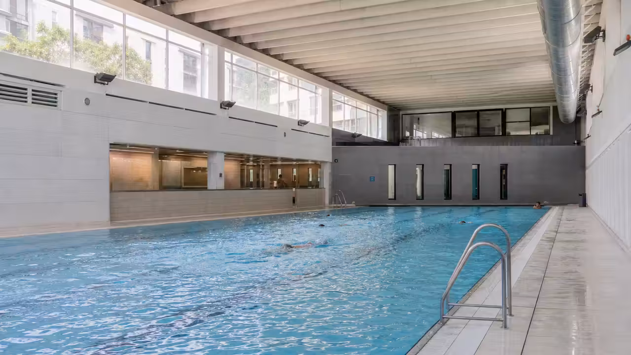 Bassin couvert rénové avec lignes d’eau, gradins discrets et lumière naturelle dans une piscine municipale