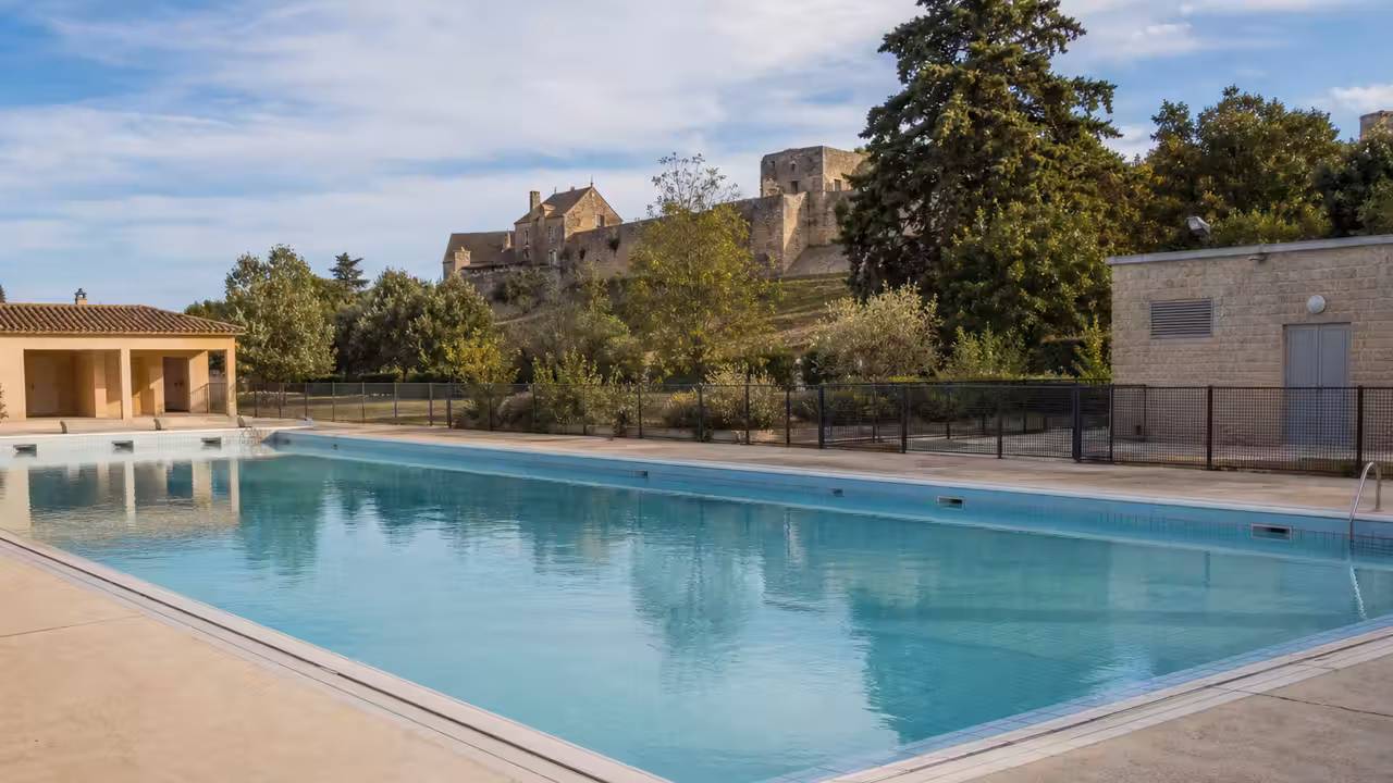 Bassin extérieur municipal vide avec plages rénovées, végétation et bâtiments techniques en arrière-plan