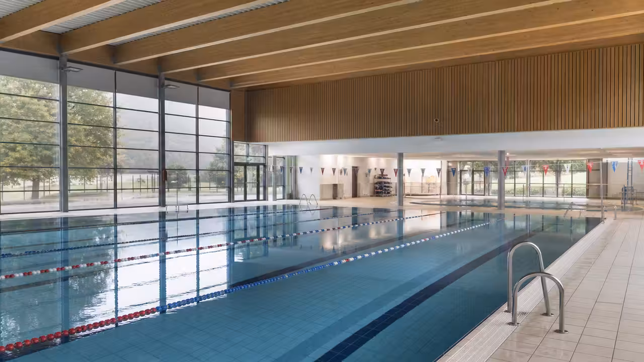 Bassin sportif lumineux d’une piscine municipale avec lignes d’eau, baies vitrées et vestiaires en arrière-plan