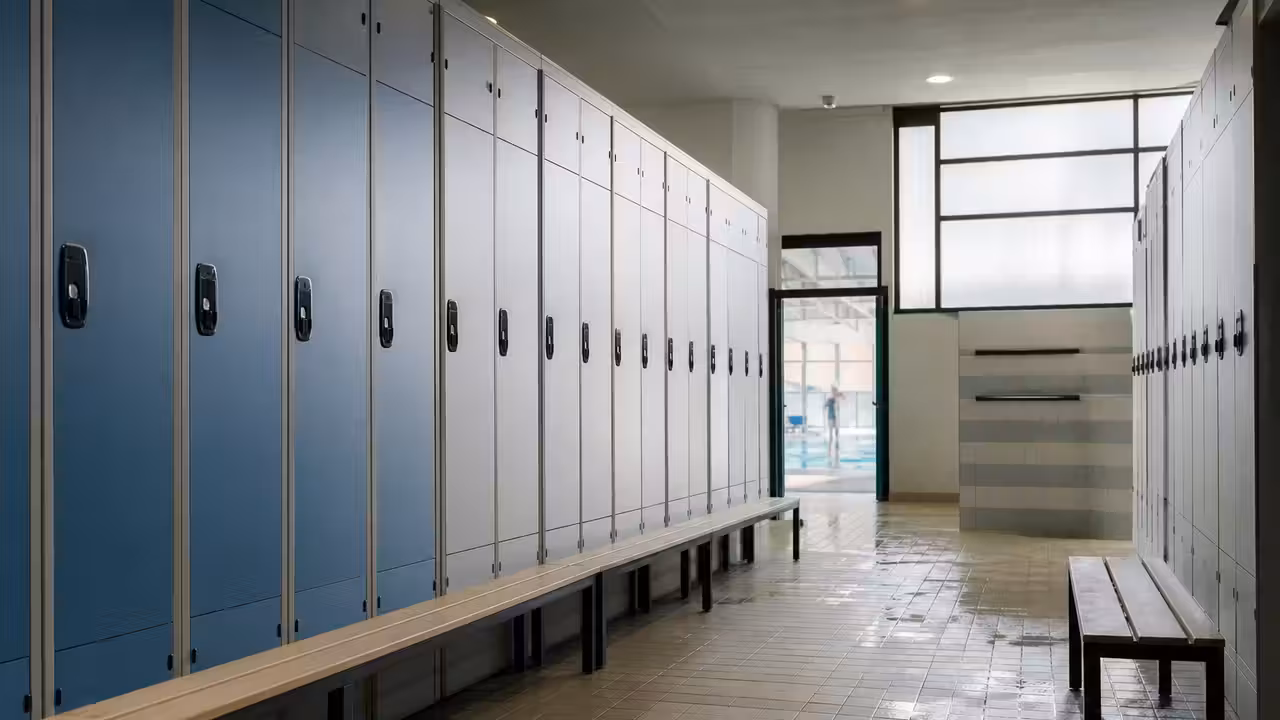 Vestiaire lumineux de piscine publique avec rangées de casiers modernes, bancs et sol antidérapant humide