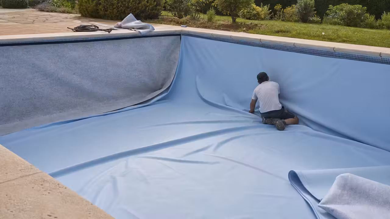 Pose d’un liner bleu dans un bassin rectangulaire, avec feutre de protection sur les parois.