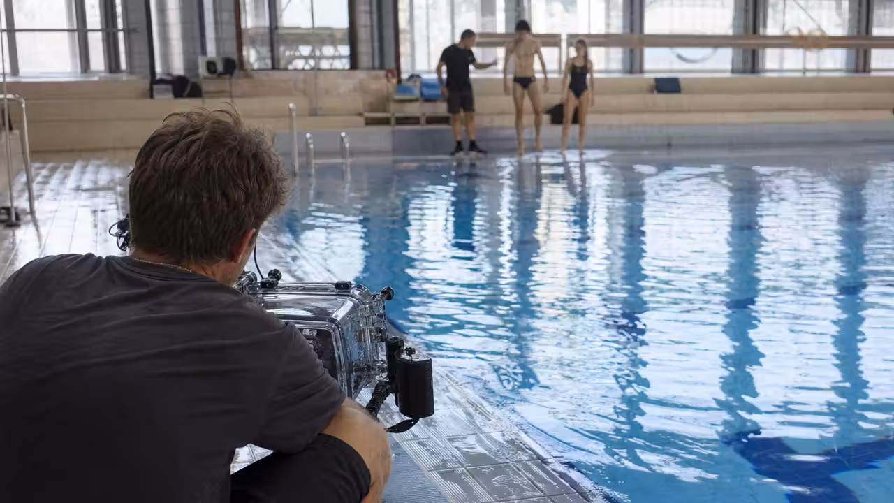 Équipe d’élèves filmant une scène près d’un bassin intérieur de piscine municipale, avec caméra protégée