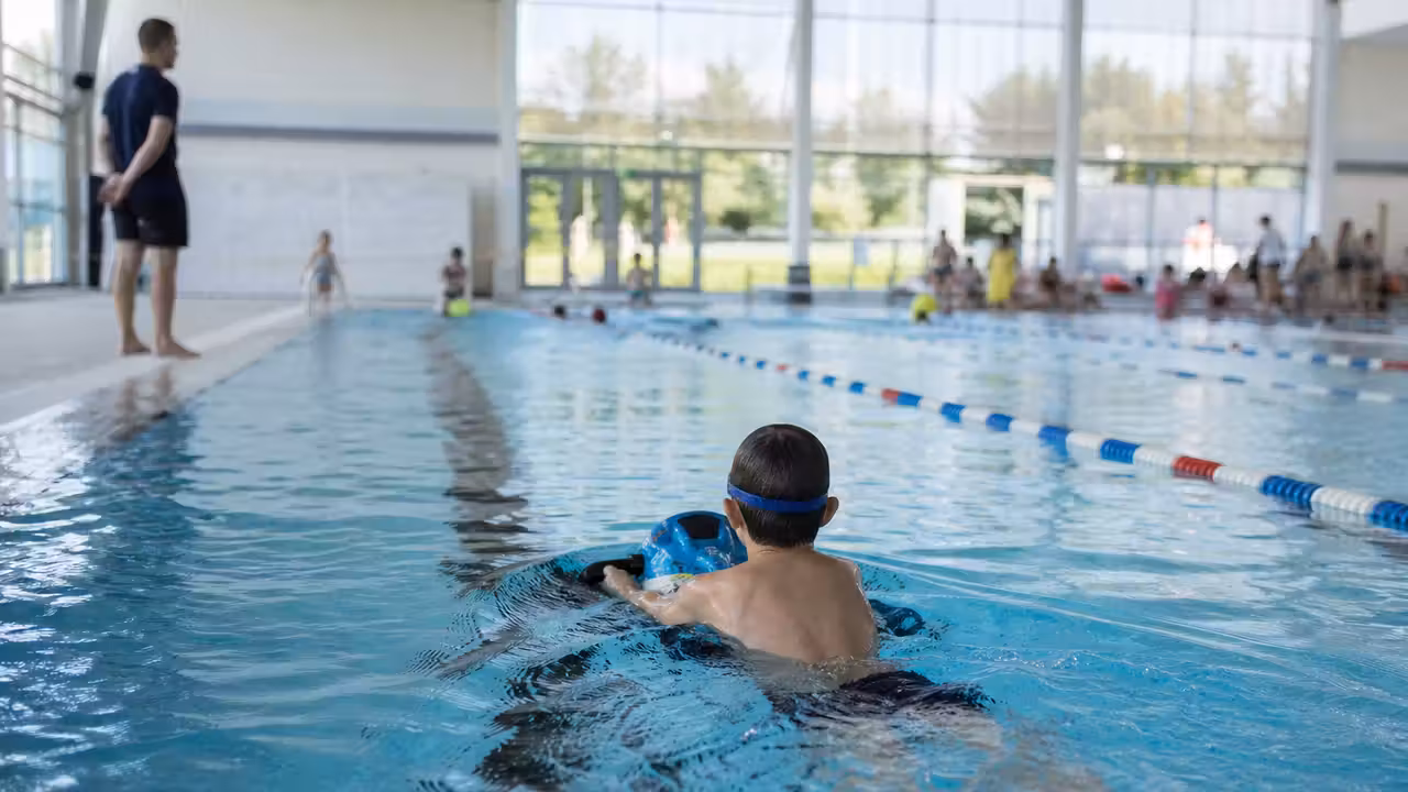 Enfant vu de dos utilisant un scooter aquatique dans un bassin sous la surveillance d’un professionnel.