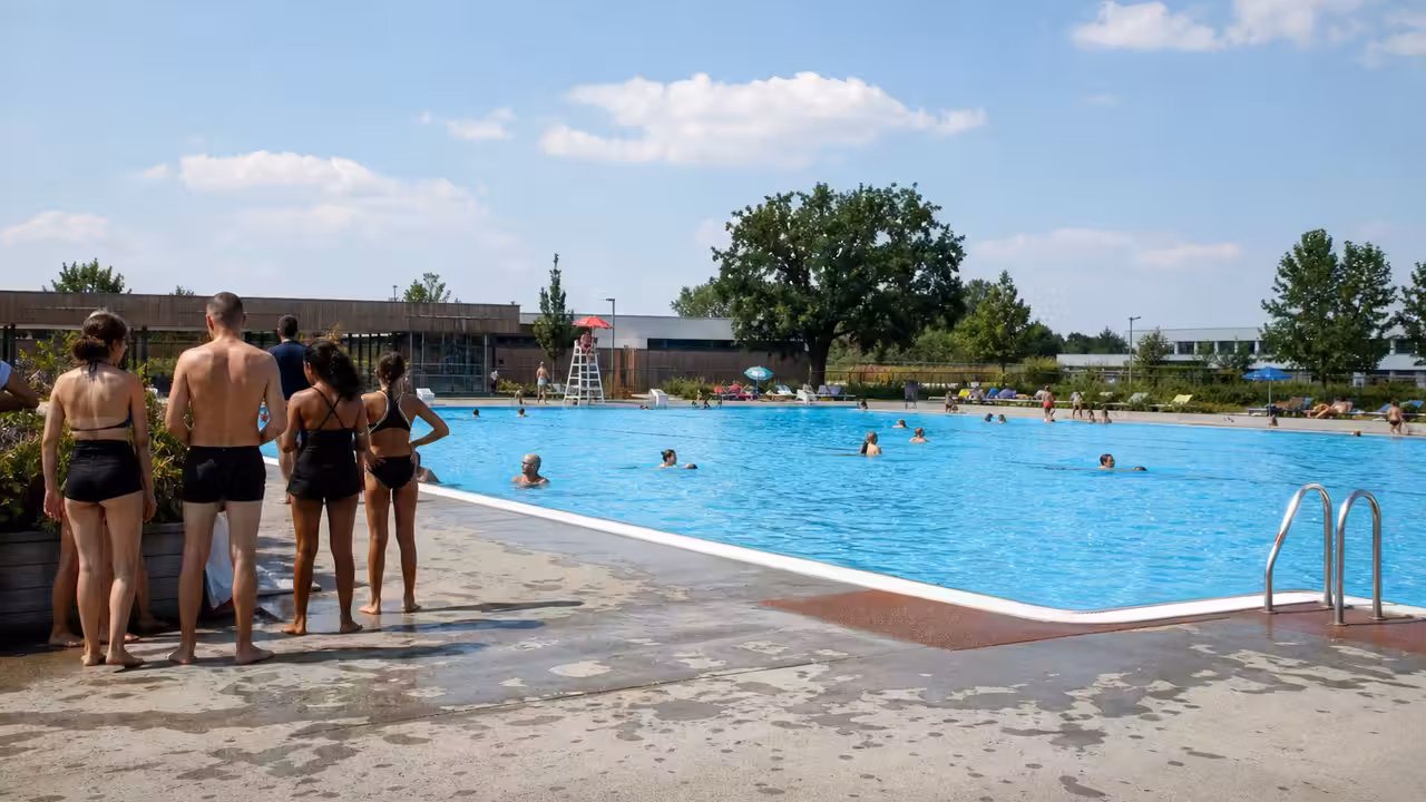 Entrée d’une piscine municipale animée en été, avec bassin extérieur et espace d’accueil en arrière-plan