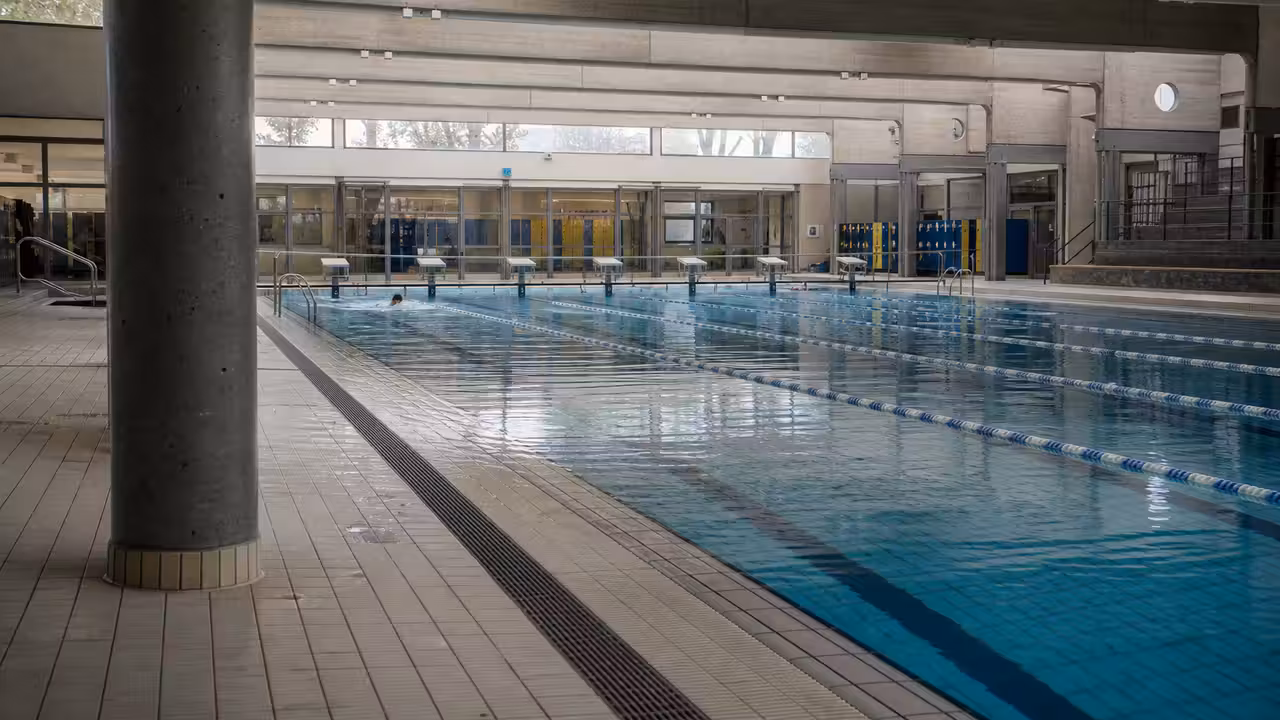 Bassin couvert municipal avec lignes d’eau vides et gradins, illustrant la tension sur les créneaux