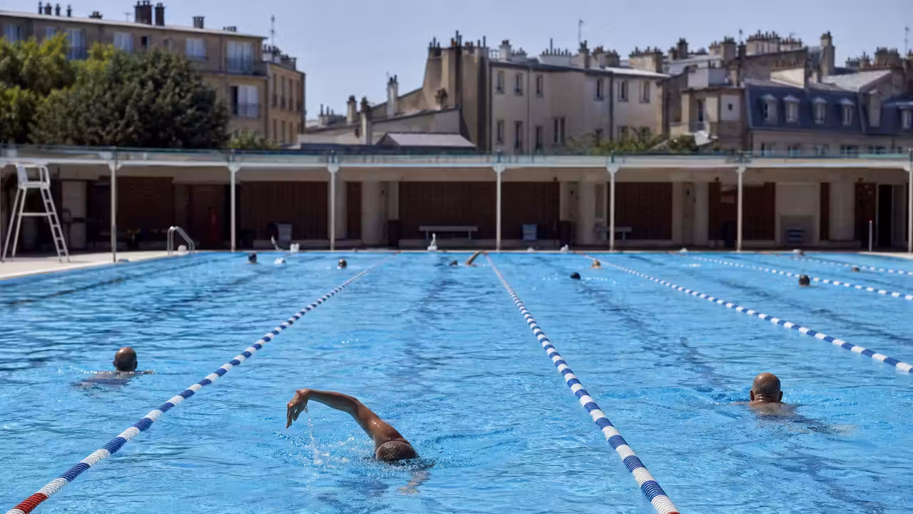 Nageurs dans un bassin municipal parisien extérieur, avec lignes d’eau et immeubles en arrière-plan