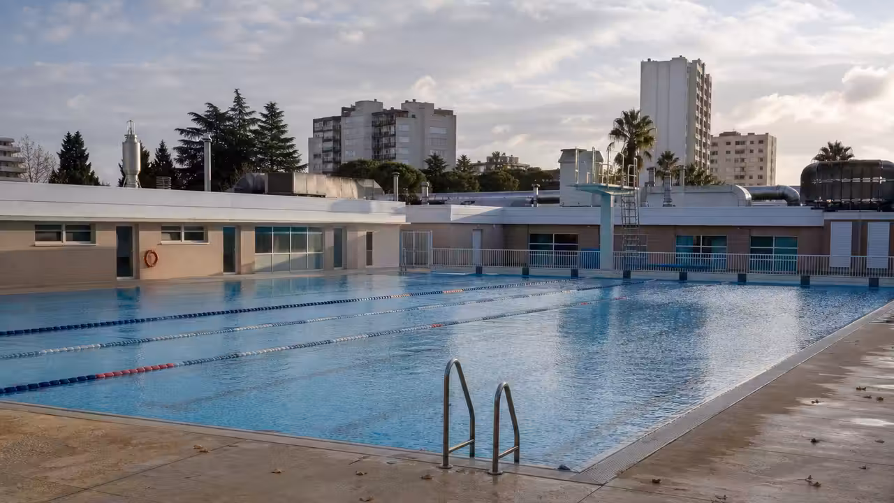 Bassin extérieur d’une piscine municipale vide en hiver, avec lignes d’eau et bâtiments techniques en arrière-plan