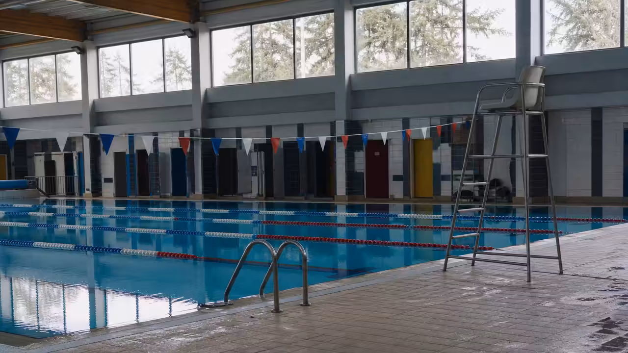 Bassin intérieur d’une piscine publique vide, lignes d’eau calmes et fauteuil de surveillance inoccupé