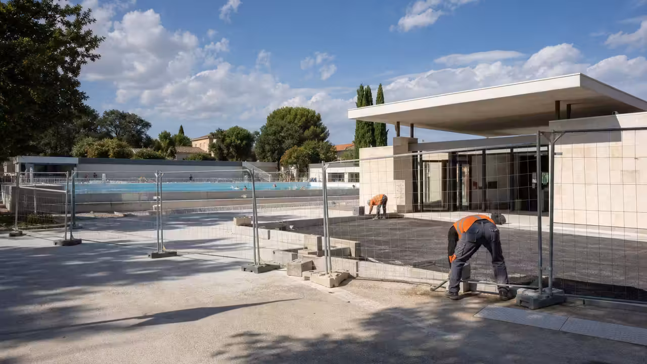Chantier de rénovation aux abords d’une piscine publique avec bassin accessible en arrière-plan