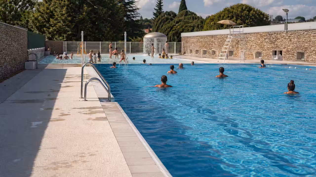 Vue estivale d’un bassin municipal extérieur avec nageurs et zone de baignade familiale à Decazeville