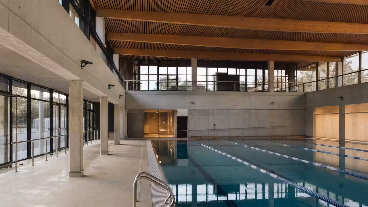 Vue extérieure d’un centre aquatique municipal moderne avec bassin visible et cheminement piétonnier arboré