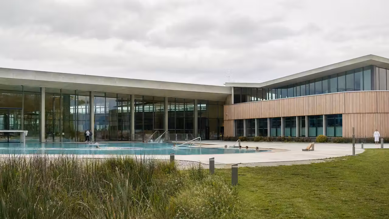 Vue extérieure d’un centre aquatique contemporain avec bassin, plages minérales et végétation de zone humide