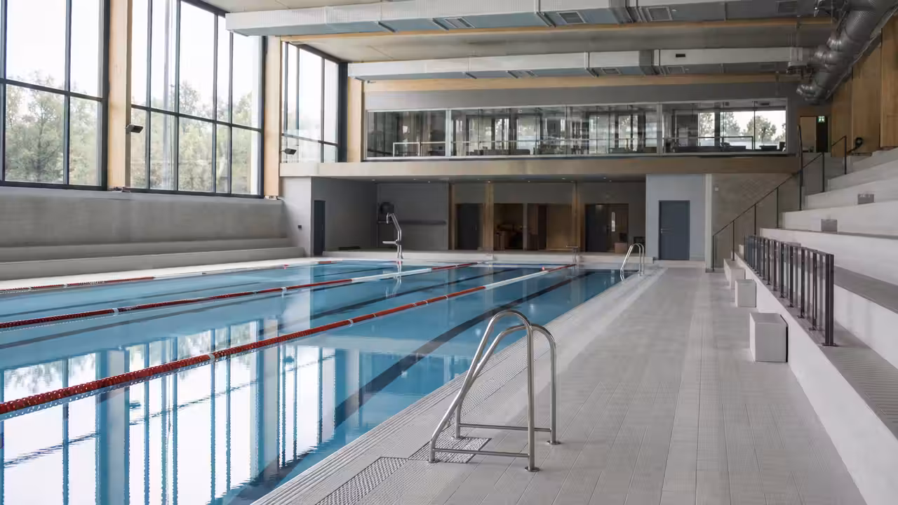 Bassin couvert rénové d’une piscine municipale, lignes d’eau et gradins vides avant la réouverture