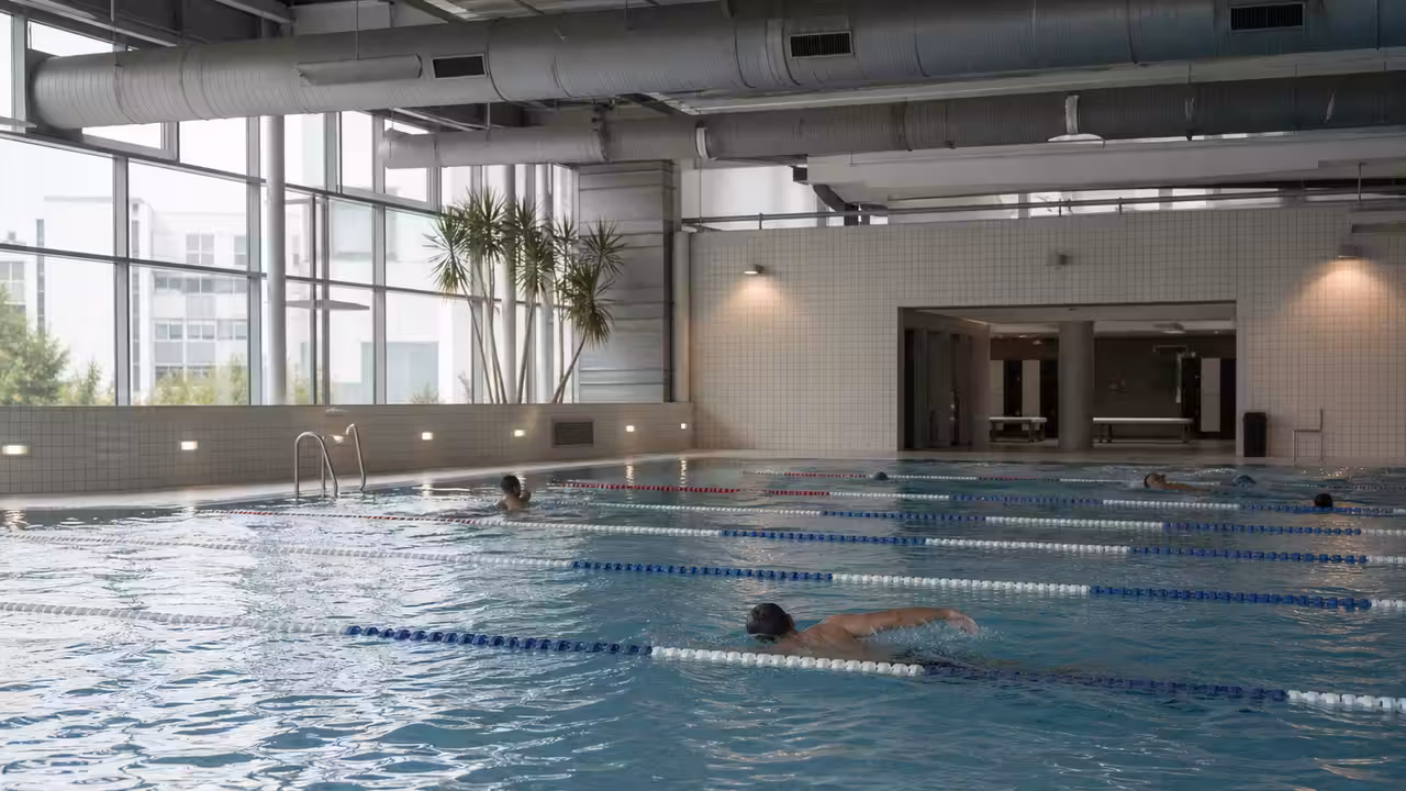 Bassin intérieur d’une piscine municipale avec lignes d’eau, vestiaires vitrés et nageurs non identifiables