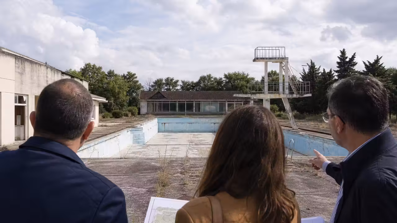 Ancien bassin extérieur vidé, entouré de plages en béton et d’arbres dans une piscine municipale française