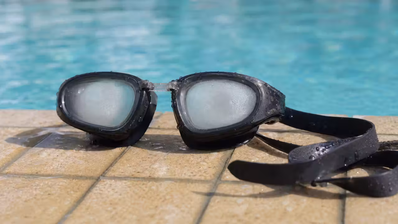 Lunettes de natation posées au bord d'une piscine, verres légèrement embués, eau turquoise en arrière-plan