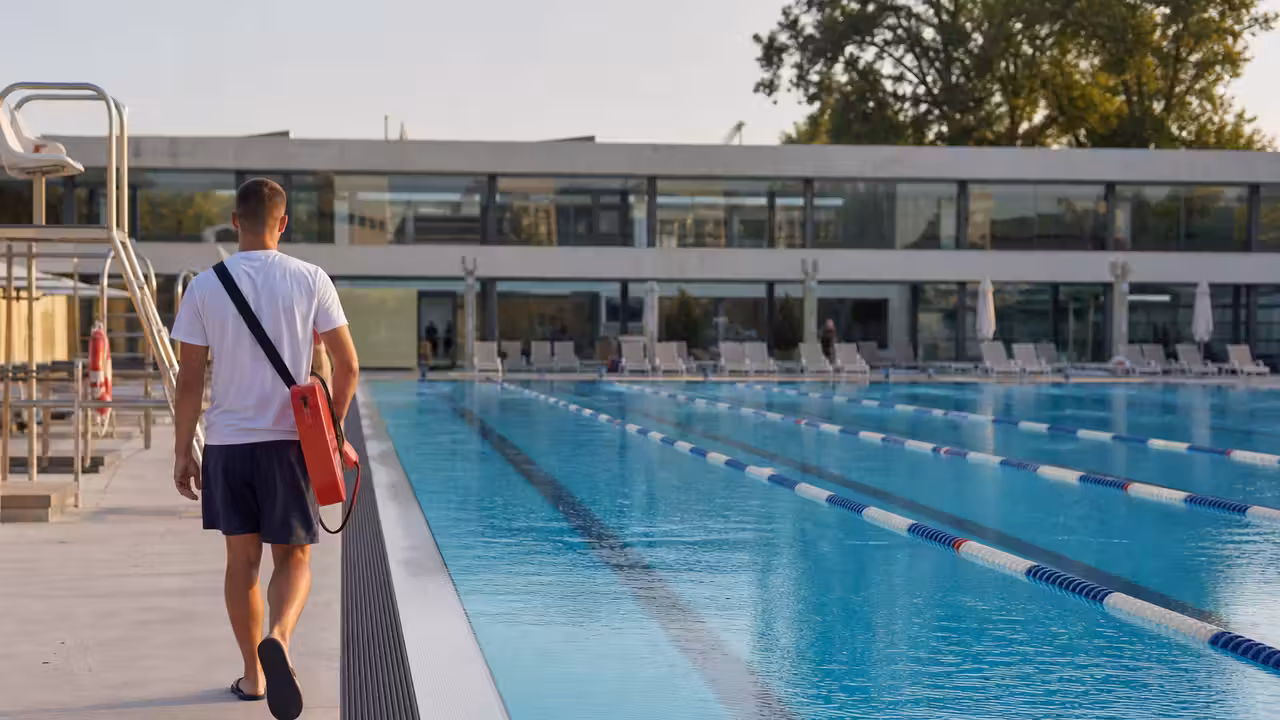 Surveillant de baignade observant un bassin extérieur animé depuis le bord d’une piscine publique