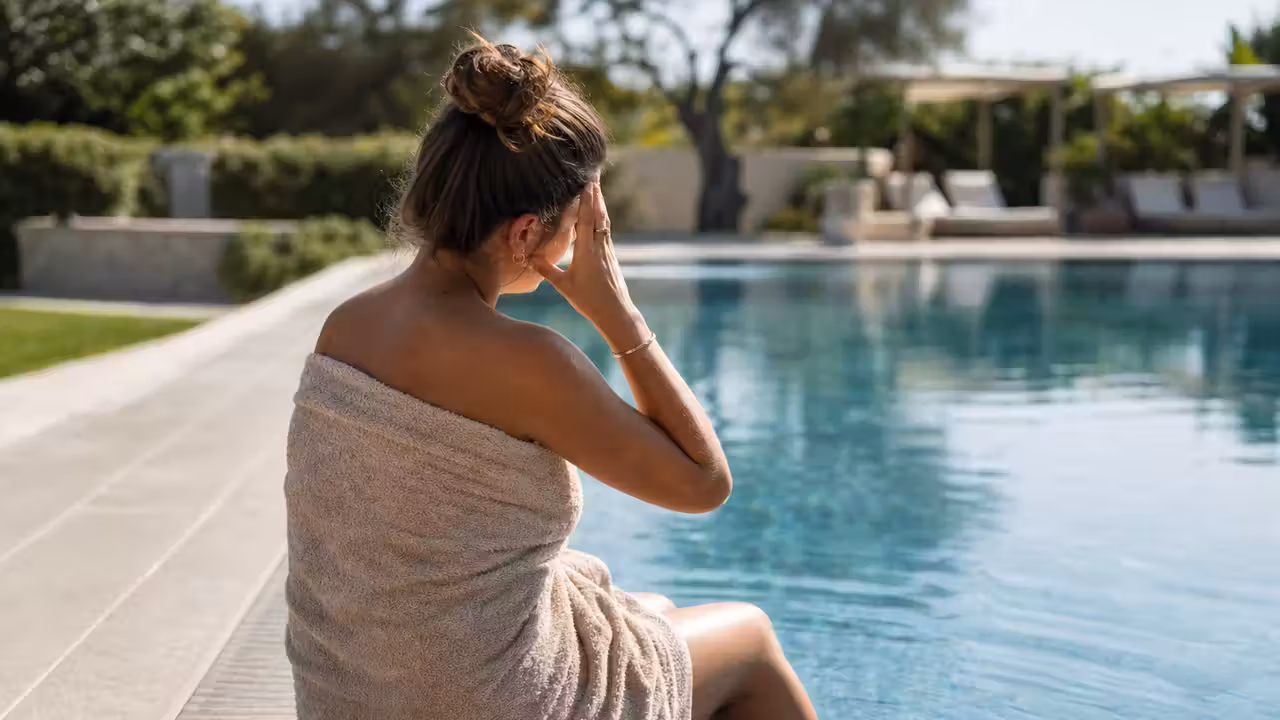 Personne assise au bord d'une piscine, serviette sur les épaules, main portée au front