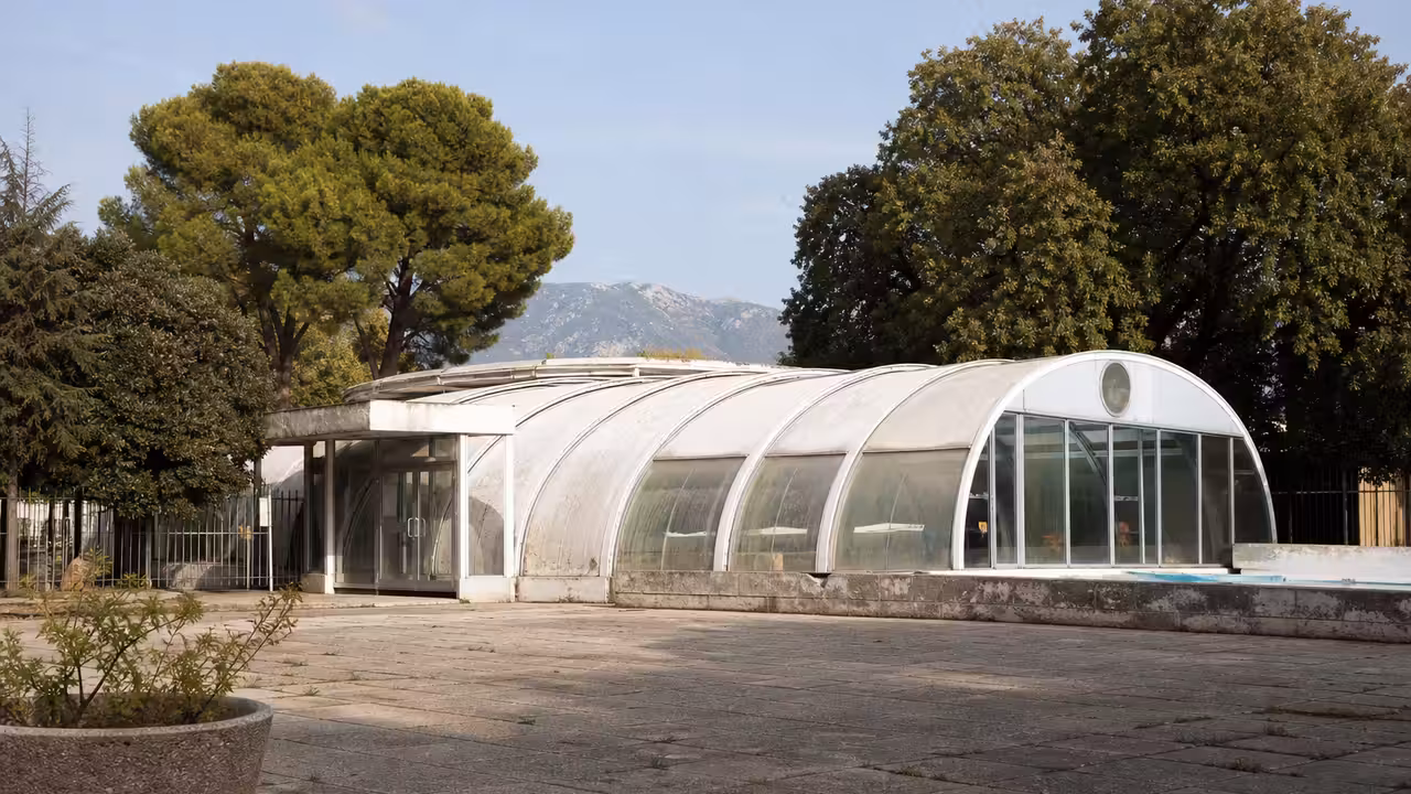 Vue extérieure d’une piscine publique à coupole circulaire, entourée d’arbres et d’équipements sportifs