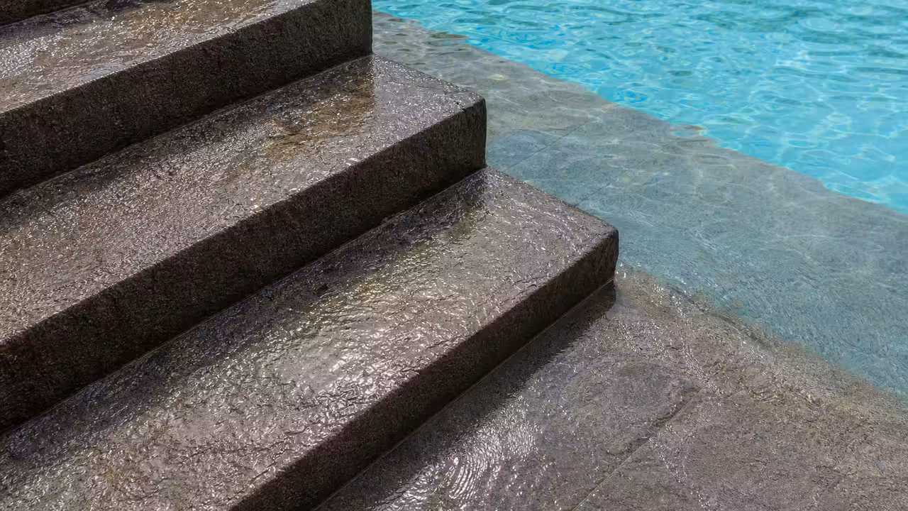 Marches d'escalier de piscine mouillées avec un revêtement texturé antidérapant, eau turquoise en arrière-plan