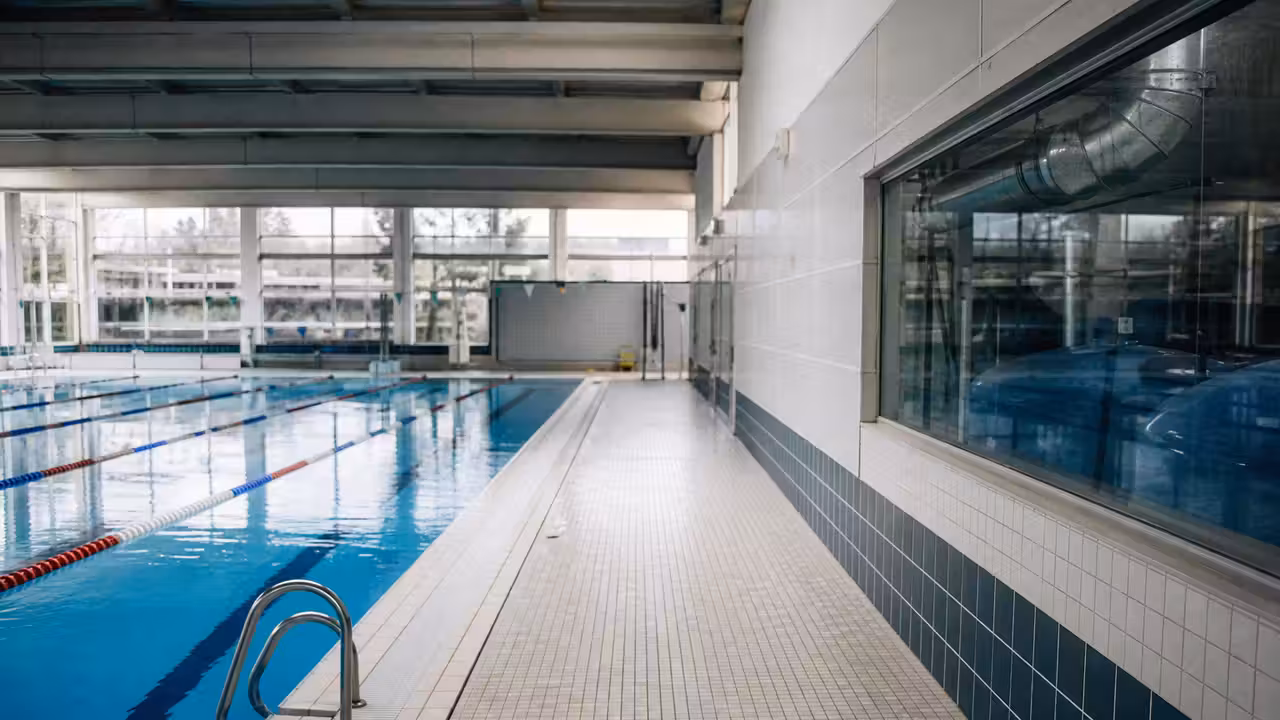 Bassin intérieur d’une piscine municipale vide, lignes d’eau immobiles et équipements techniques en arrière-plan