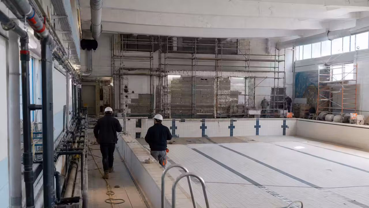 Bassin intérieur en rénovation avec échafaudages et réseaux techniques apparents dans une piscine publique