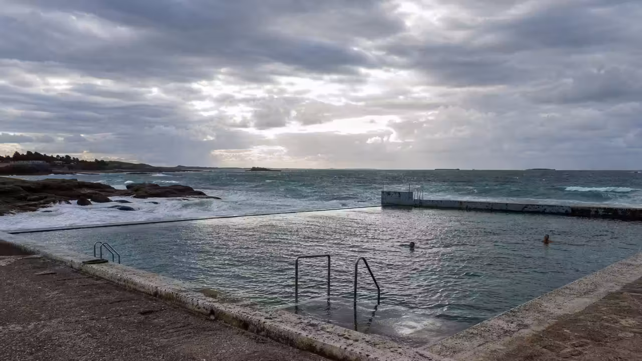 Bassin de baignade d’eau de mer en bord de mer, avec gradins minéraux et vagues au loin