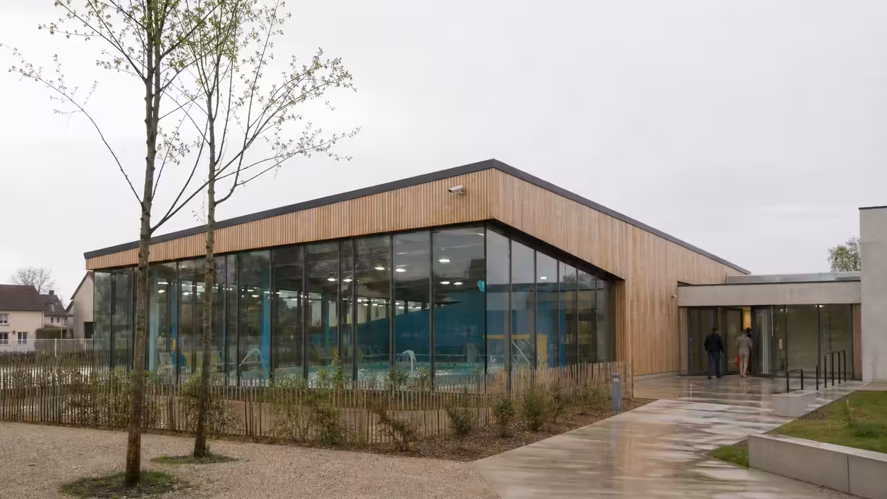Vue extérieure d’un centre aquatique contemporain avec bassin couvert et parvis, dans une petite ville française