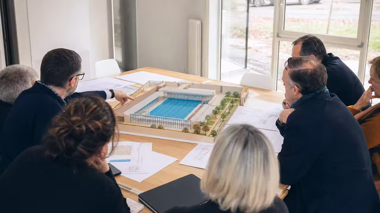 Élus et techniciens examinant la maquette d’un projet de piscine municipale lors d’une réunion de travail